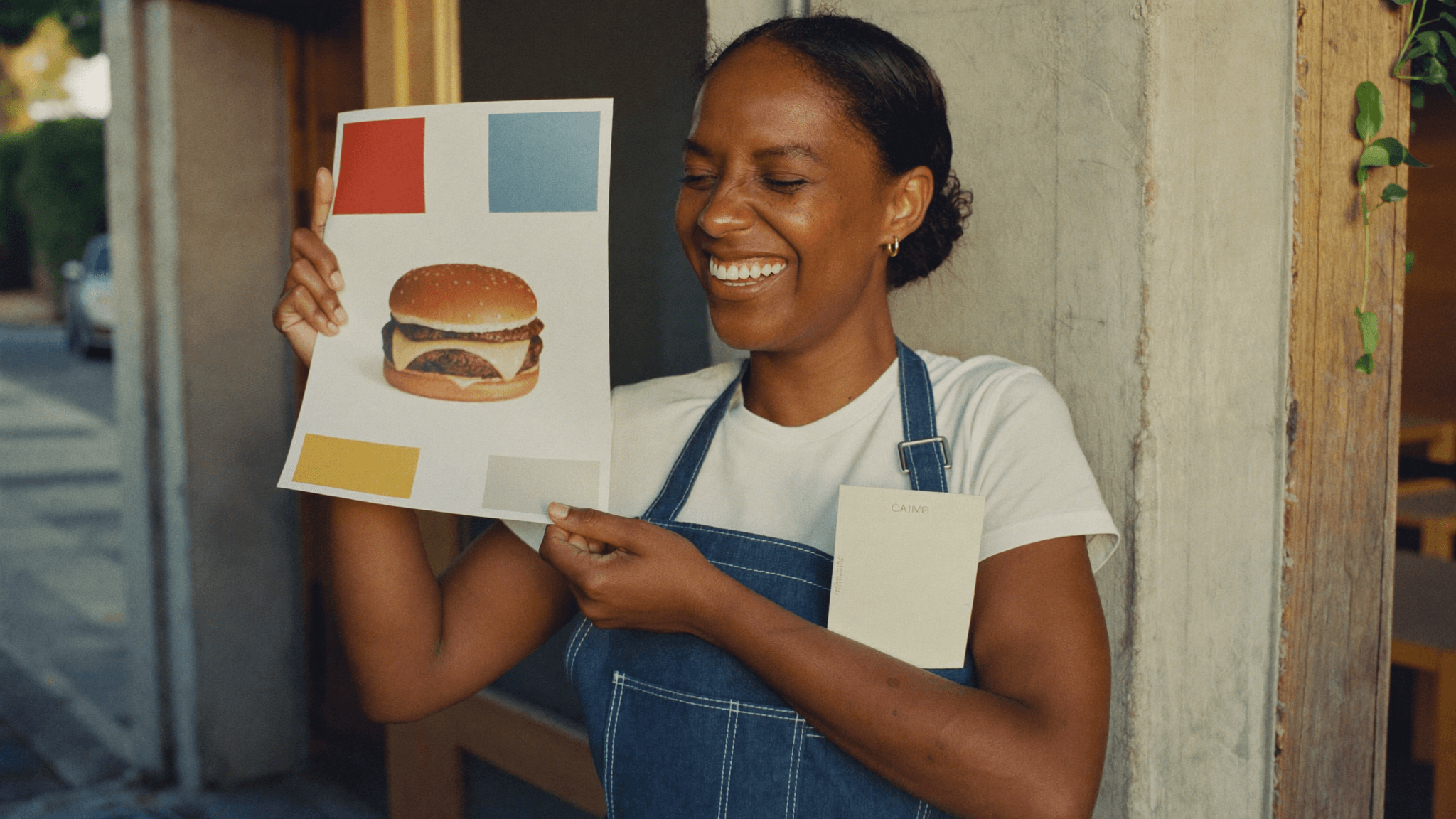 Dona de hamburgueria na porta do salão segurando com orgulho o cartaz impresso da promoção